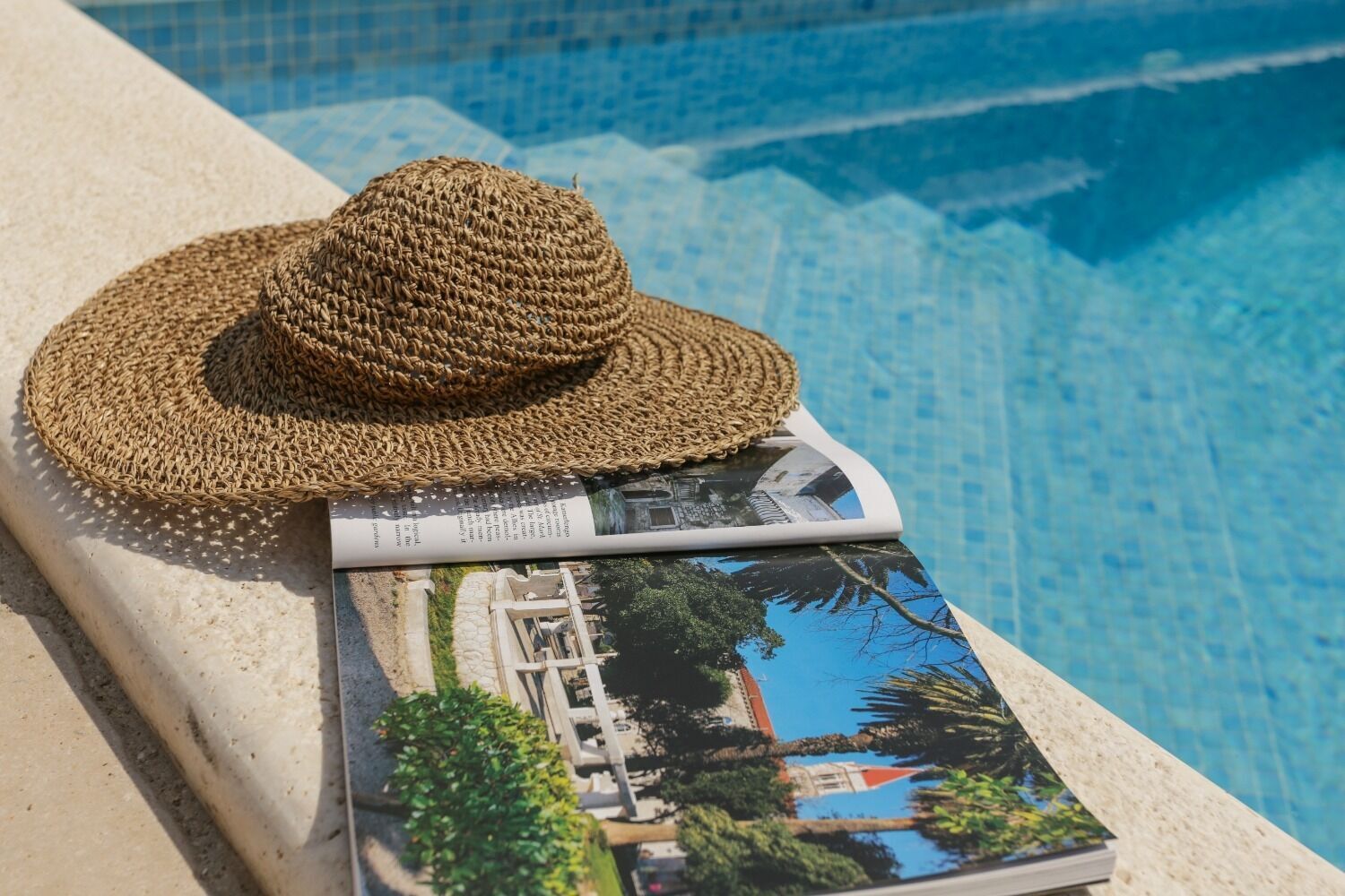 A straw hat and a magazine on a poolside ledge.