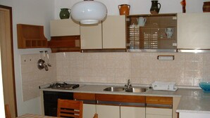Eine kompakte Küche mit Gasherd, doppelter Spüle, Holzschränken und einem Esstisch mit kariertem Tischläufer.