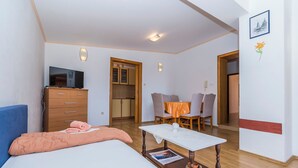 Et moderne hotelværelse med seng, kommode, fjernsyn, spiseplads med bord og stole samt et tekøkken.