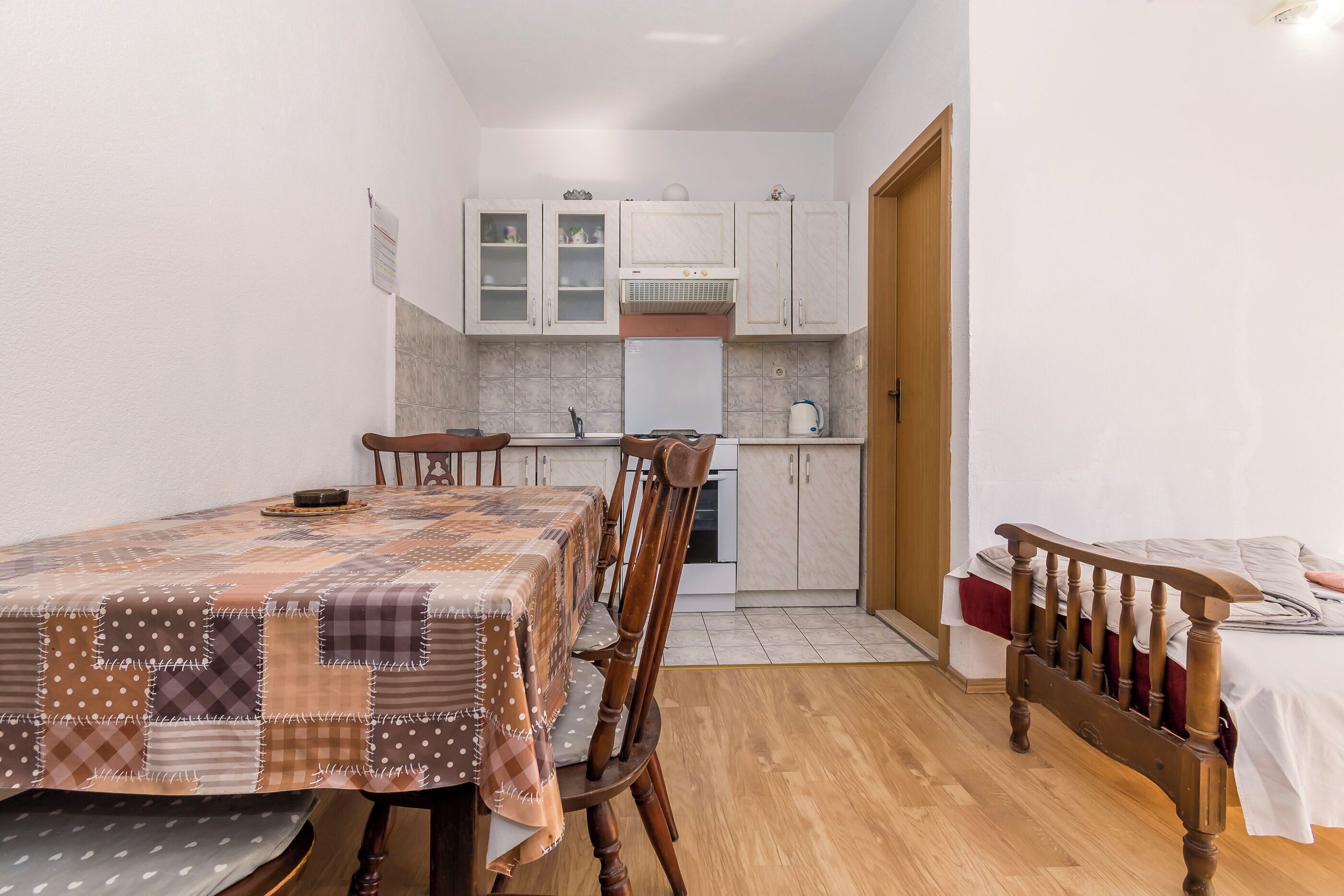 A compact kitchen with white cabinets, a white refrigerator, and a wooden dining table with a patchwork tablecloth.