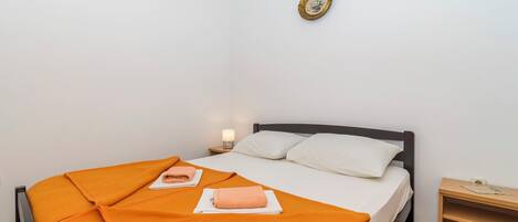Ein ordentlich bezogenes Bett mit einer orangefarbenen Decke, ein Nachttisch mit einer Lampe und ein gerahmtes Bild an der Wand.