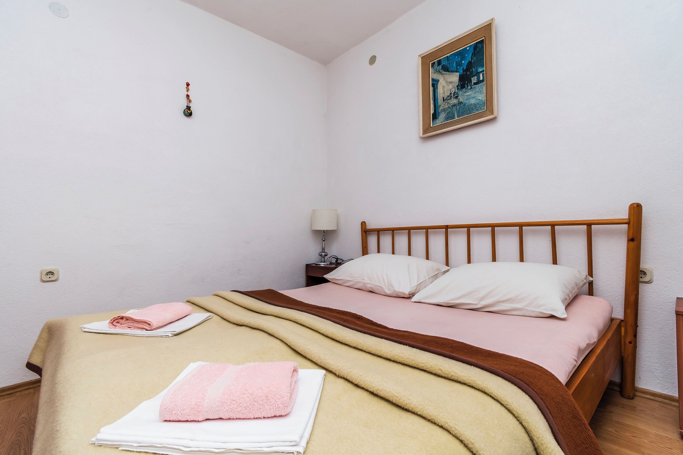 Un lit bien fait, avec une tête de lit en bois, une lampe de chevet et un tableau accroché au mur.