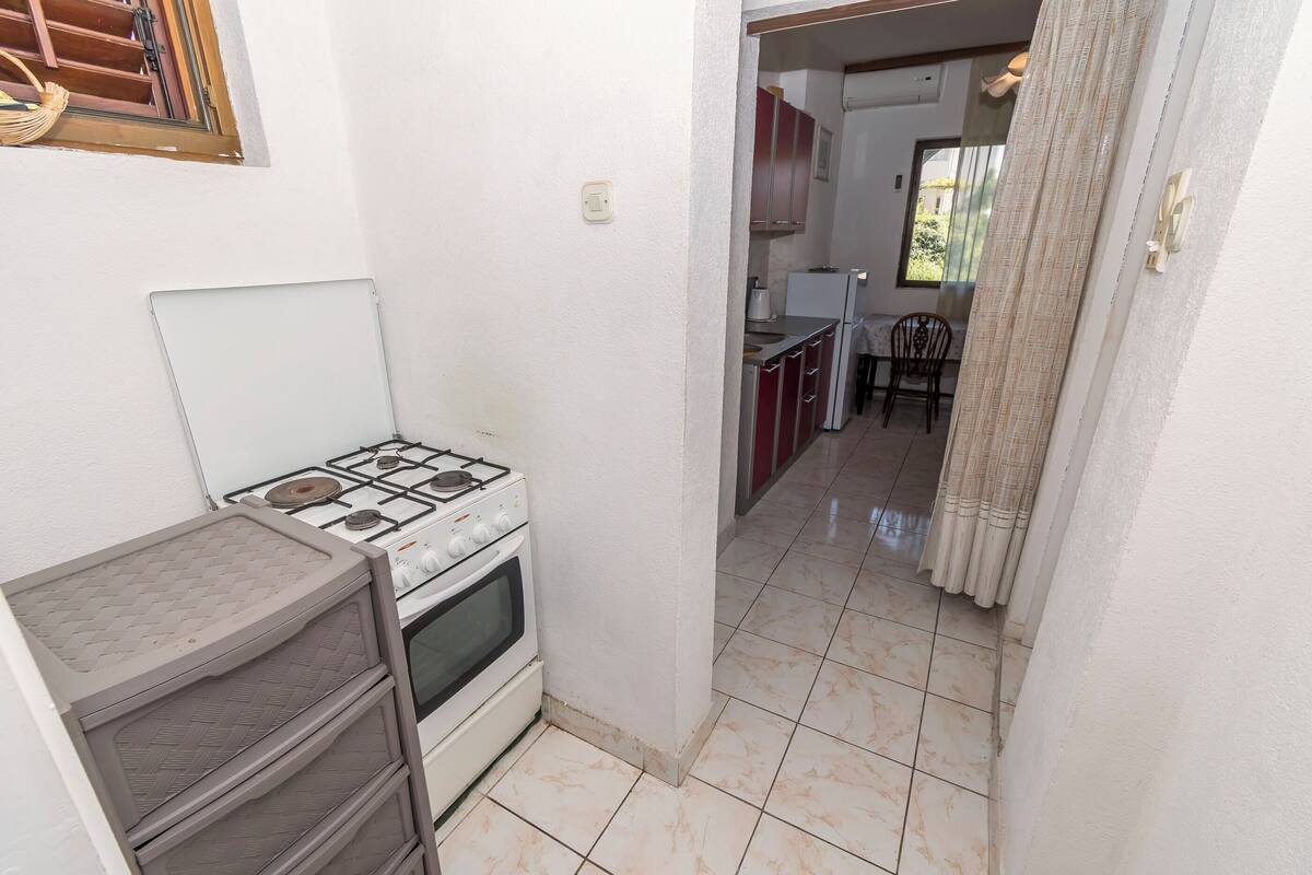 A compact kitchen with a gas stove, oven, and a small cabinet. A doorway leads to a dining area with a table and chairs.