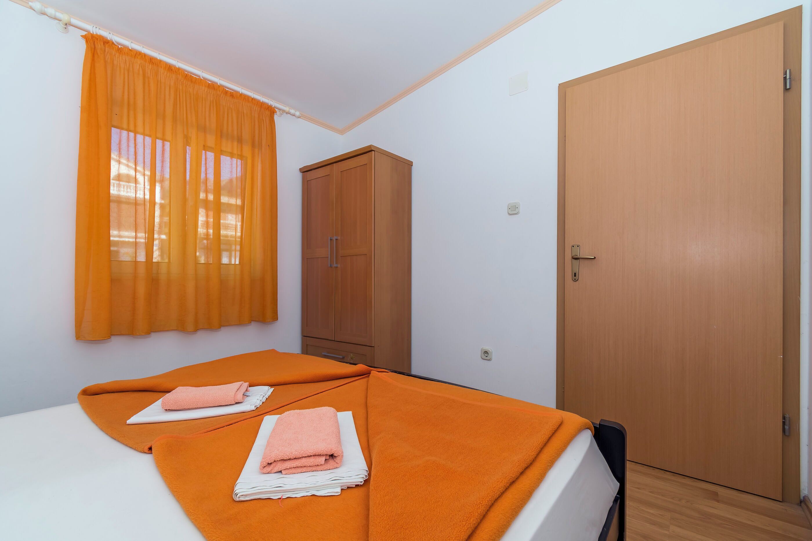 Une chambre avec deux lits, une literie orange, une armoire en bois et une porte.