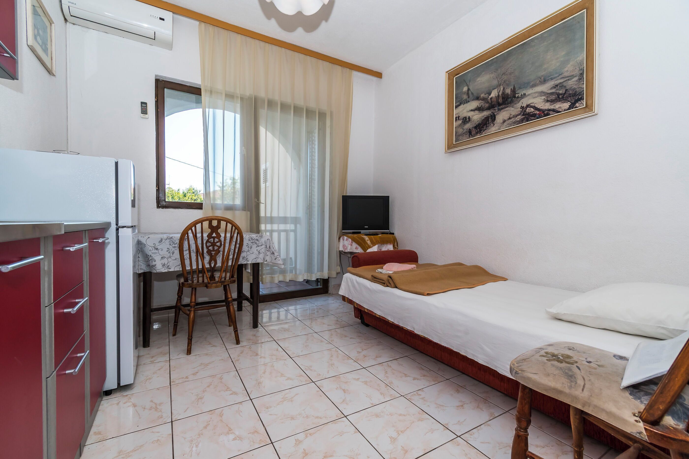 Una stanza piccola e pulita con un letto, una scrivania, una sedia, una TV e un frigorifero.
