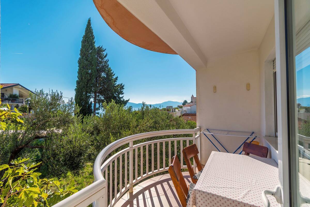 A balcony with a table and chairs, overlooking a garden and a mountain.