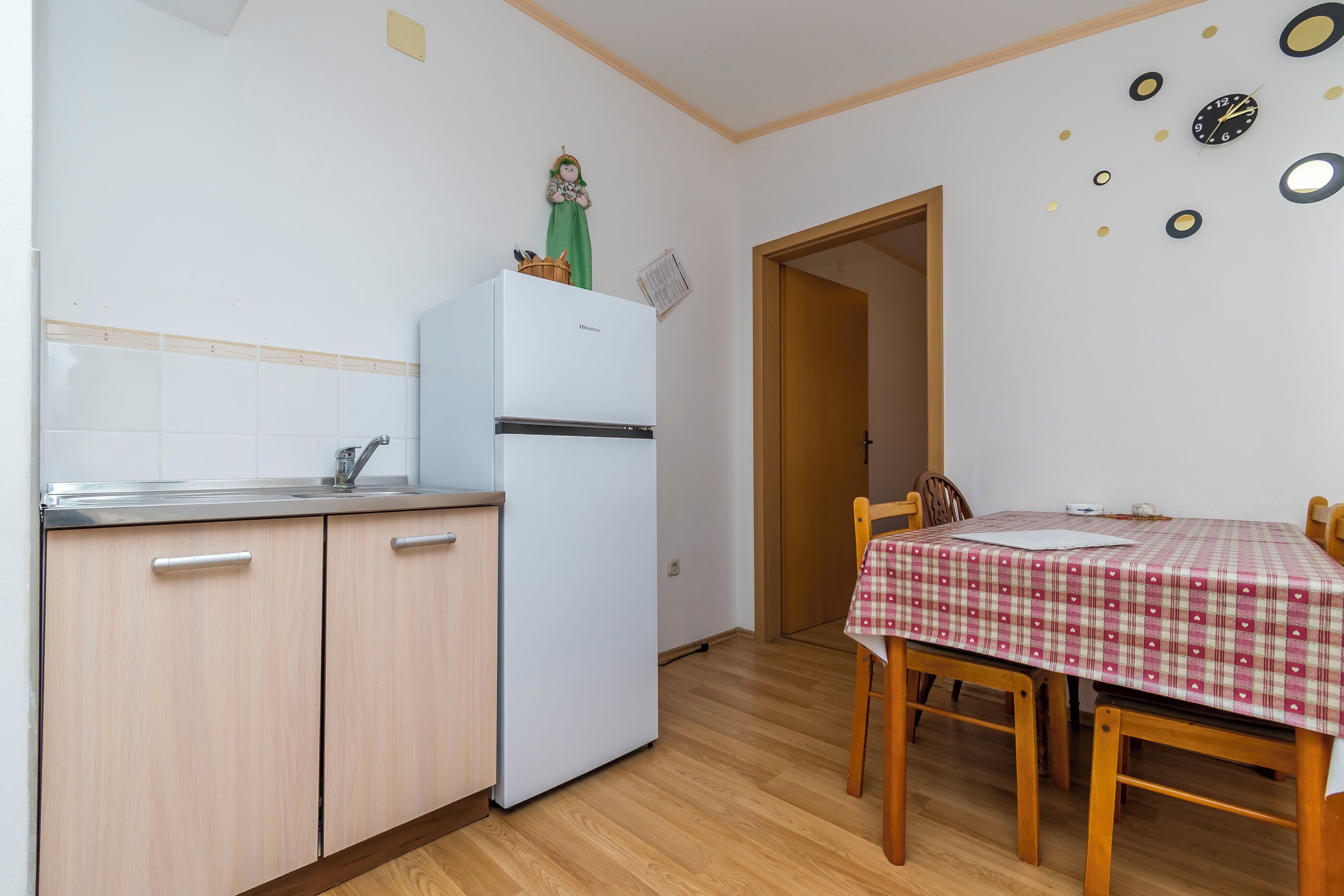 Eine kleine Küche mit Kühlschrank, Holzschränken und einem Esstisch mit kariertem Tischläufer.