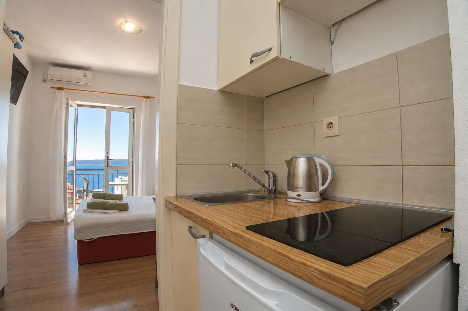A compact kitchen with a built-in stove, a kettle, and a sink.