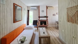 A room with a bed, a small table, a chair, a fireplace, and a mirror on the wall. - Apartments Tiho (Podgora)