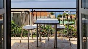 A balcony with a table and two chairs, overlooking a body of water and buildings. - Apartments Tiho (Podgora)