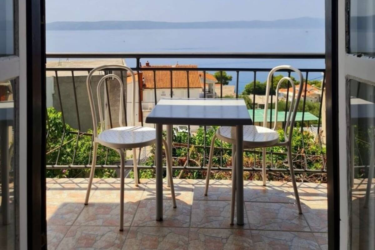 A balcony with a table and two chairs, overlooking a body of water and buildings.