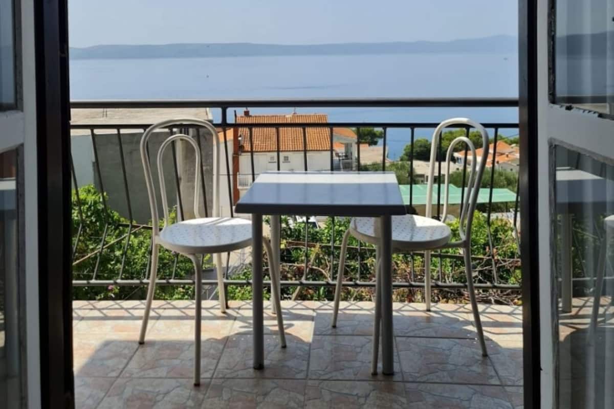 A balcony with two white tables and chairs, a view of the sea, and a tiled floor.