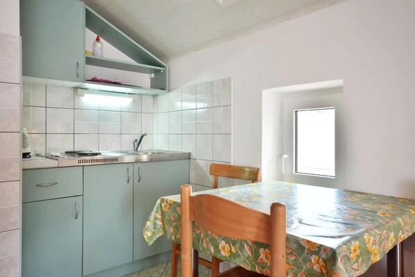 A compact kitchen with light green cabinets, a single sink, and a dining table with a floral tablecloth. - Apartment Toma (Omis)