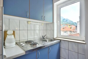 A kitchen with blue cabinets, a white countertop, a built-in stove, and a window with a view of buildings and mountains.
