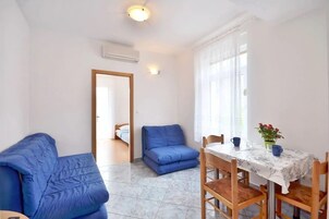 A room with a bed, a blue sofa, a dining table with chairs, and a window with curtains.