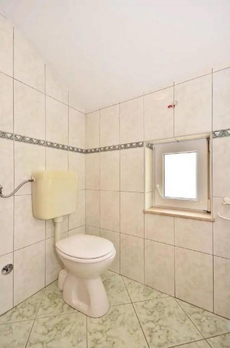 A small bathroom with a toilet, a window, and tiled walls.