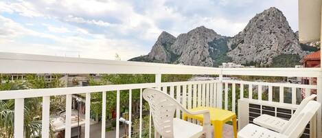 Ein Balkon mit weißen Geländern, einem gelben Tisch und weißen Stühlen.