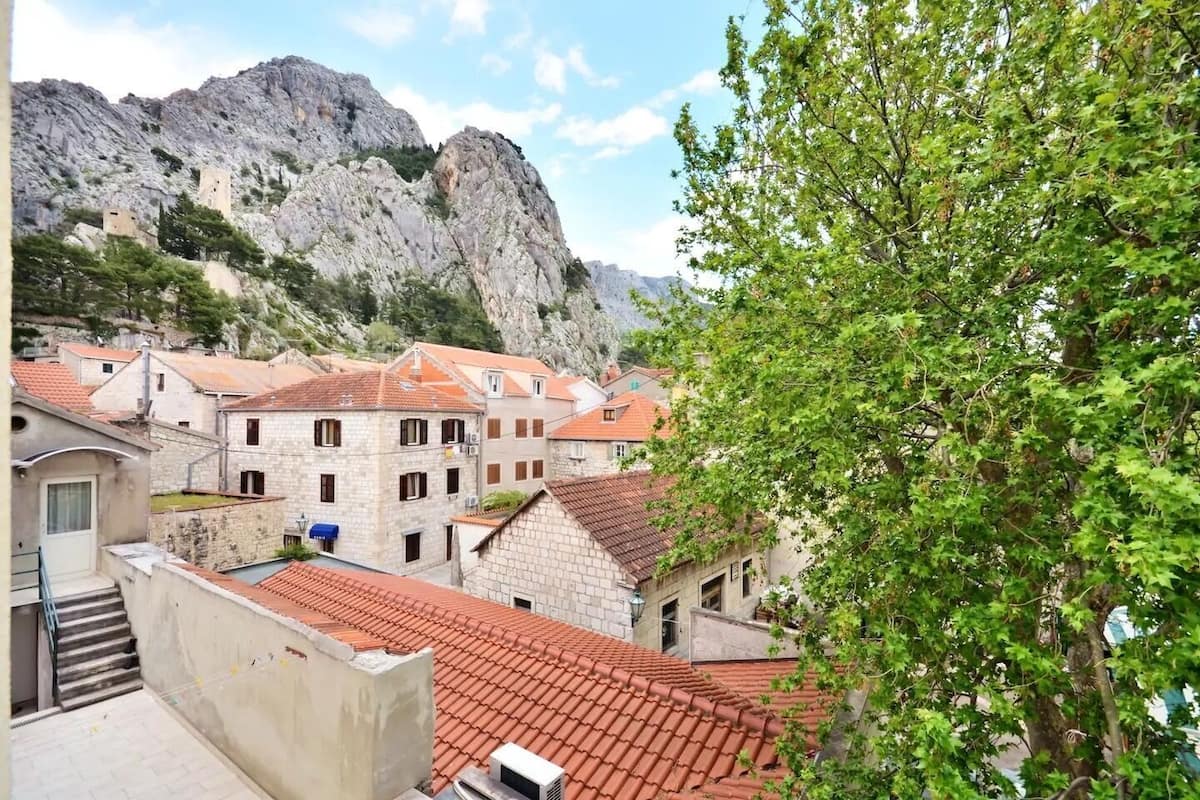 A traditional stone building with red-tiled roofs, set against a mountainous backdrop.