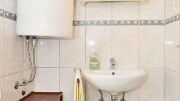 Casa de banho com sanita, lavatório e prateleira.