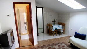 A room with a wooden floor, a dining table with chairs, a sofa, a TV, and a shower area. - Apartments Nik (Gradac)