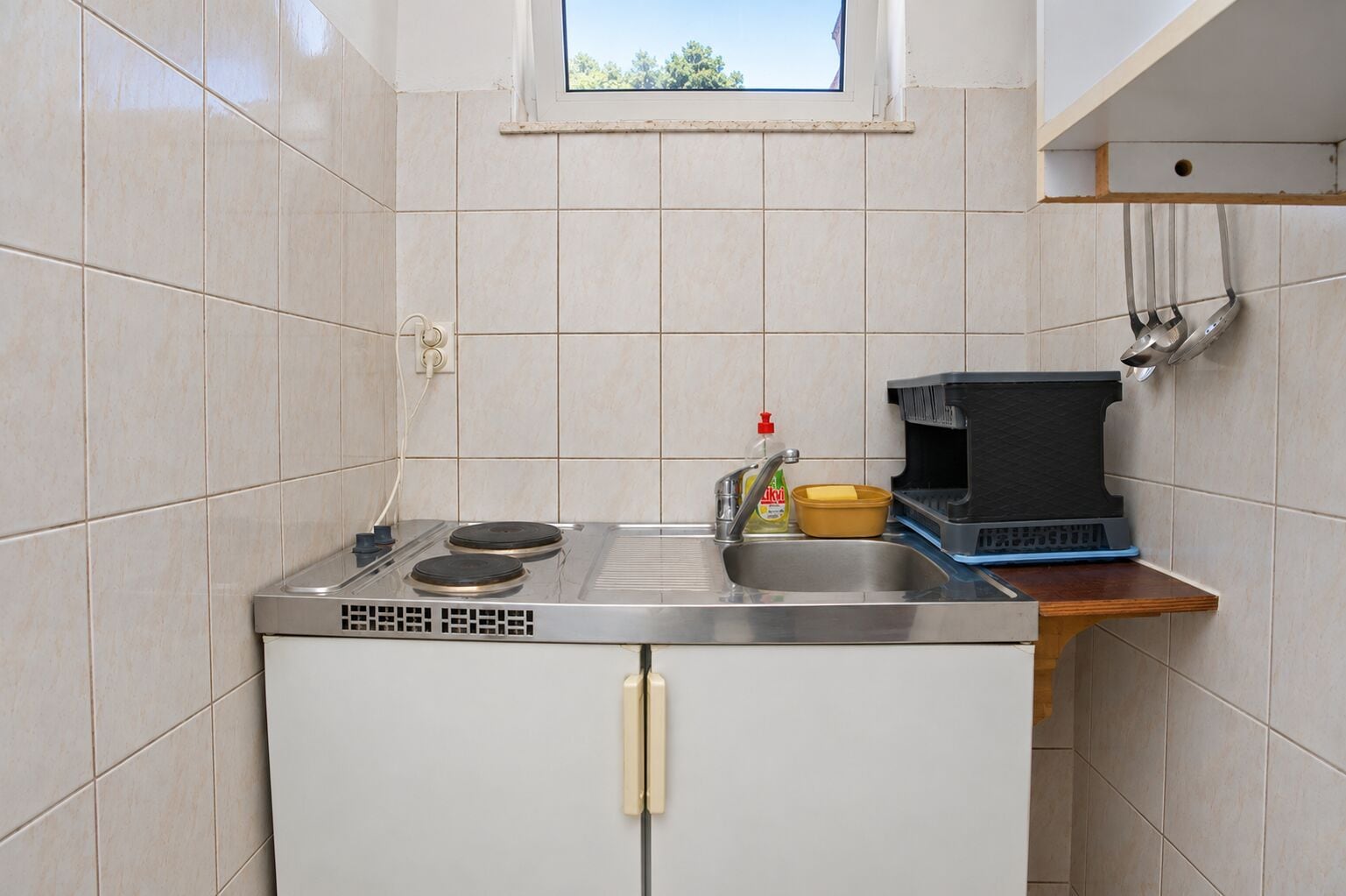 Eine kompakte Küche mit eingebautem Herd, einem Spülbecken und einem kleinen Fenster über der Arbeitsfläche.