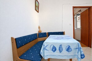 A room with a wooden bench and a table covered with a light blue tablecloth featuring sea shells and starfish. - Apartments Nik (Gradac)