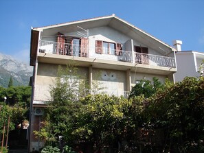 A two-story building with balconies, a mountain backdrop, and surrounding greenery. - Apartments Nik (Gradac)