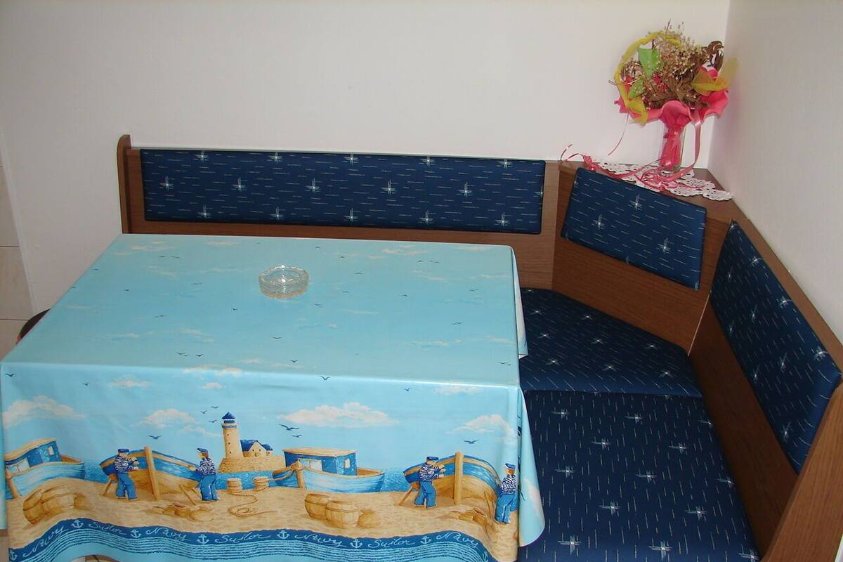 A dining table with a nautical-themed tablecloth, a wooden bench with a blue cushion, and a vase with flowers on the table's right side.