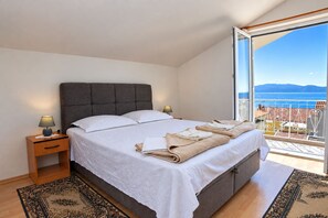 A bedroom with a large bed, bedside lamps, a nightstand, a view of the sea, and a balcony with a railing. - Apartments Nik (Gradac)