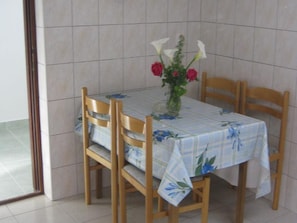 Ein Esstisch mit einer blumigen Tischdecke, umgeben von Holzsesseln und einer Vase mit Blumen.