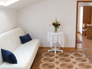 A room with a white sofa, a small round table with a lace tablecloth, and a vase with flowers. - Apartments Nik (Gradac)