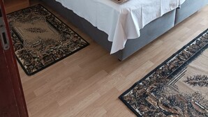 A neatly made bed with white linens and a grey headboard, a bedside table with a lamp, and a patterned rug on the floor. - Apartments Nik (Gradac)