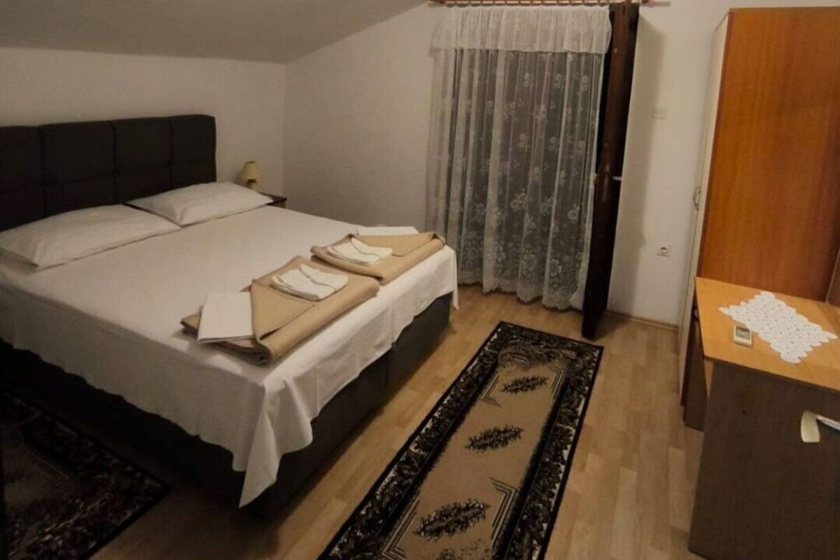 A bedroom with a bed, a nightstand, a dresser, a window with curtains, and an air conditioning unit.