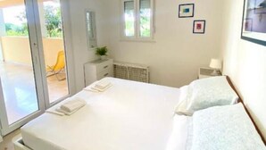 A bedroom with a bed, a nightstand, a window, and a door leading to an outdoor area. - Apartment Gojko (Podgora)
