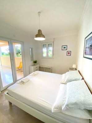 A bedroom with a bed, a nightstand, a window, and a door leading to an outdoor area. - Apartment Gojko (Podgora)