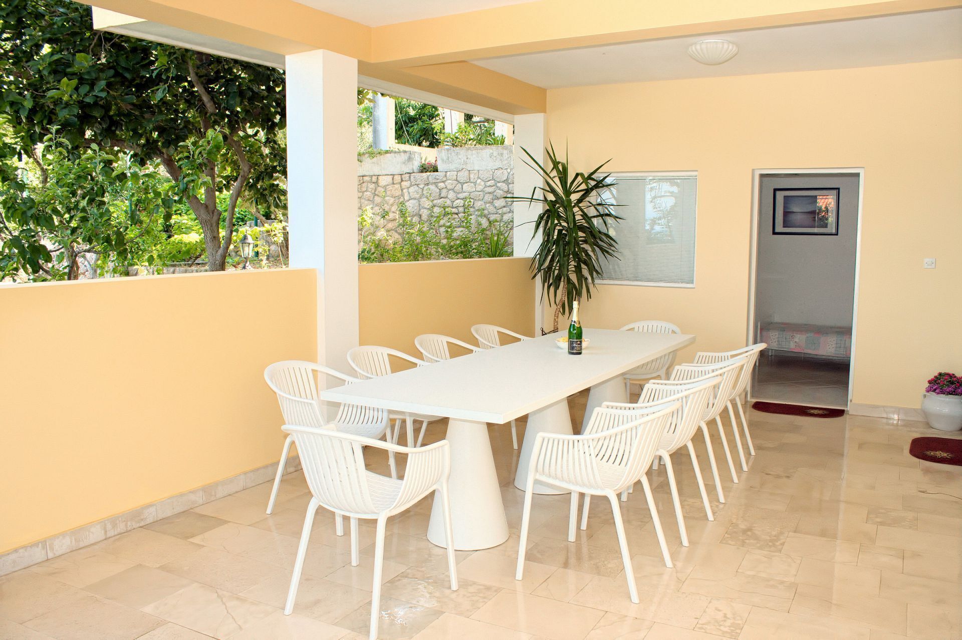 A dining area with a white table and chairs, a potted plant, and a stone wall.