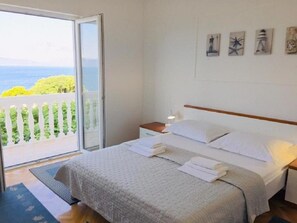A bedroom with a bed, a nightstand, a lamp, and a view of the sea through a sliding door. - Apartment Gojko (Podgora)