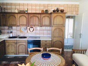 A kitchen with wooden cabinets, a sink, stove, and a dining area with a table and chairs. - Apartment Gojko (Podgora)
