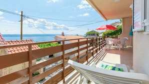 A balcony with a view of the sea, a red umbrella, and a table with chairs. - Apartment Mirja (Omis)
