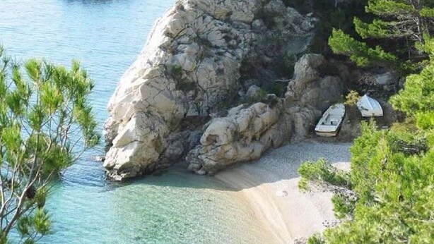 A rocky coastal area with clear water, boats, and pine trees. - Apartment Mirja (Omis)
