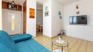 A living room with a blue sofa, a TV, and a dining area with chairs and a table. - Apartment Mirja (Omis)