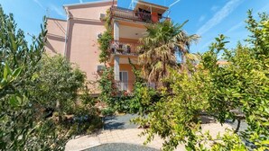 Un edifici d'alguns pisos amb balcons, envoltat de vegetació exuberant i un cel clar.