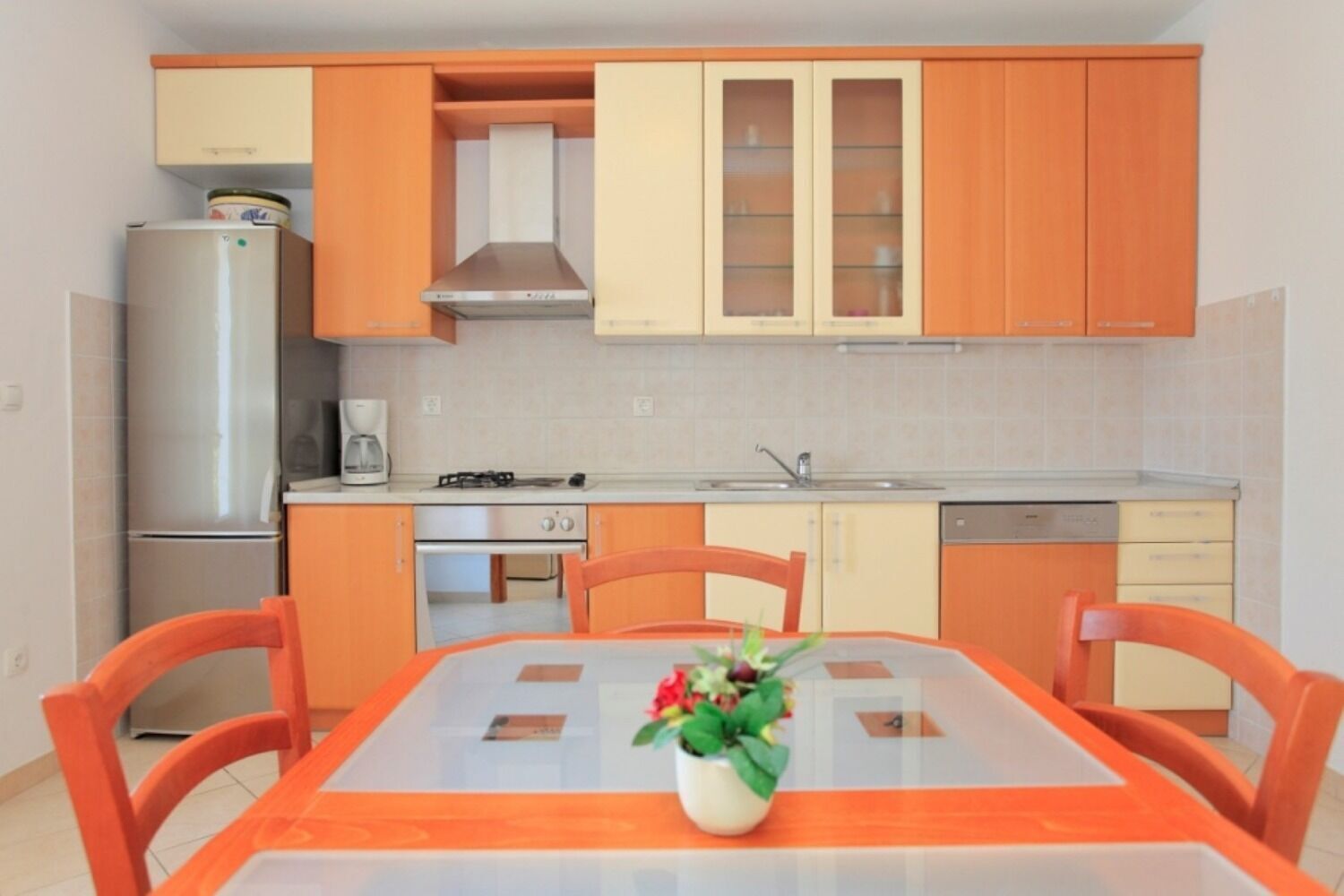 A compact kitchen with a dining table, chairs, a refrigerator, a stove, and cabinets.