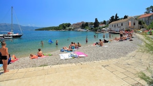Una spiaggia con persone che prendono il sole e nuotano, un'imbarcazione a vela e edifici sullo sfondo.
