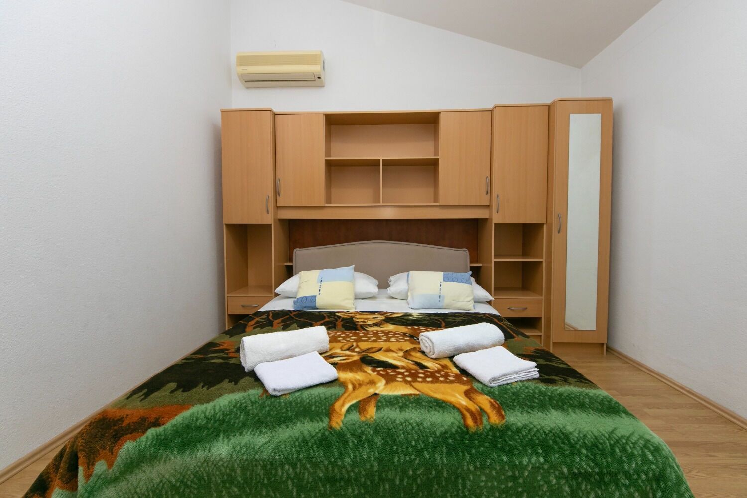 A bedroom with a bed, a headboard, a wardrobe, and a wall-mounted air conditioner.