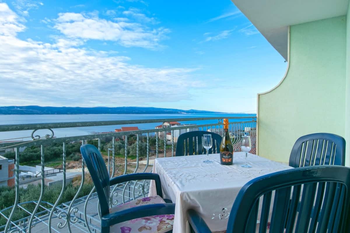 A balcony with a table set for two, overlooking a body of water and distant hills.