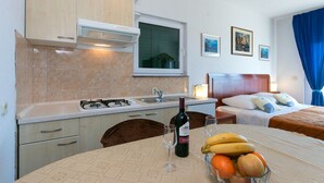 A compact hotel room with a kitchenette, a bed with a wooden headboard, and a dining area with a table set for two. - Apartments Marko (Brela)