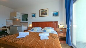 A hotel room with a bed, a desk, a kitchenette, and a large window with curtains. - Apartments Marko (Brela)