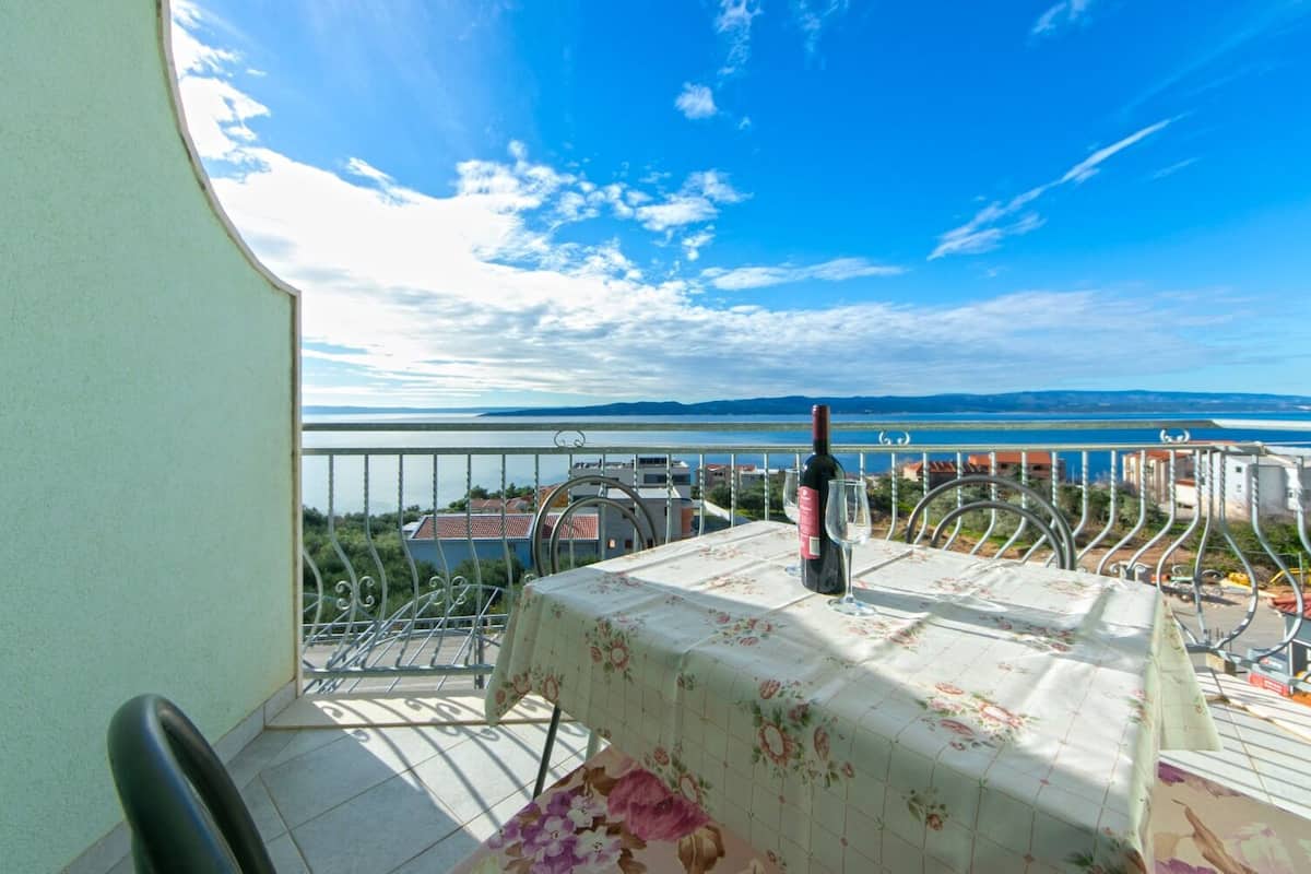 A balcony with a table set for two, overlooking a scenic view of a lake and distant mountains.