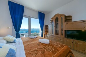 A hotel room with a large bed, a TV, wooden cabinets, and a balcony with a view of the sea. - Apartments Marko (Brela)